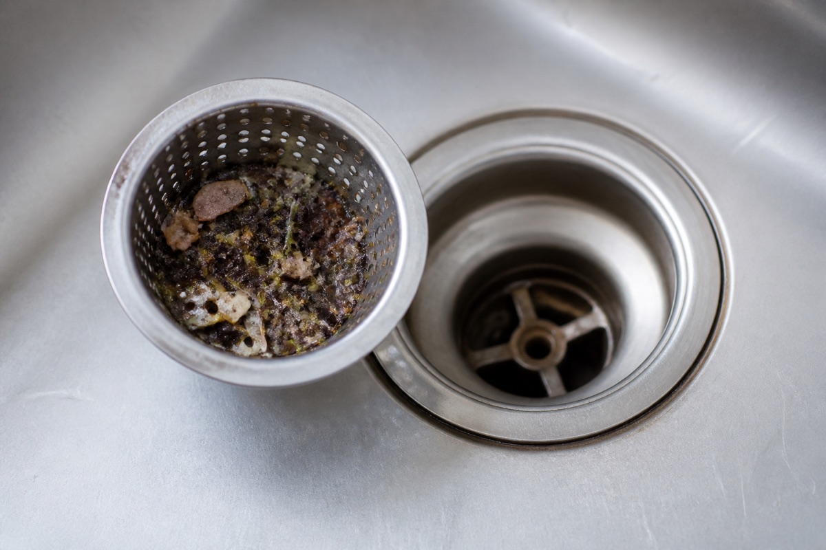 Kitchen sink drain with the strainer lifted out showing accumulated debris in the basket