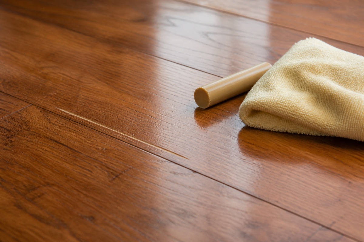 Hardwood floor with a visible surface scratch, a wax repair stick and cloth resting beside it