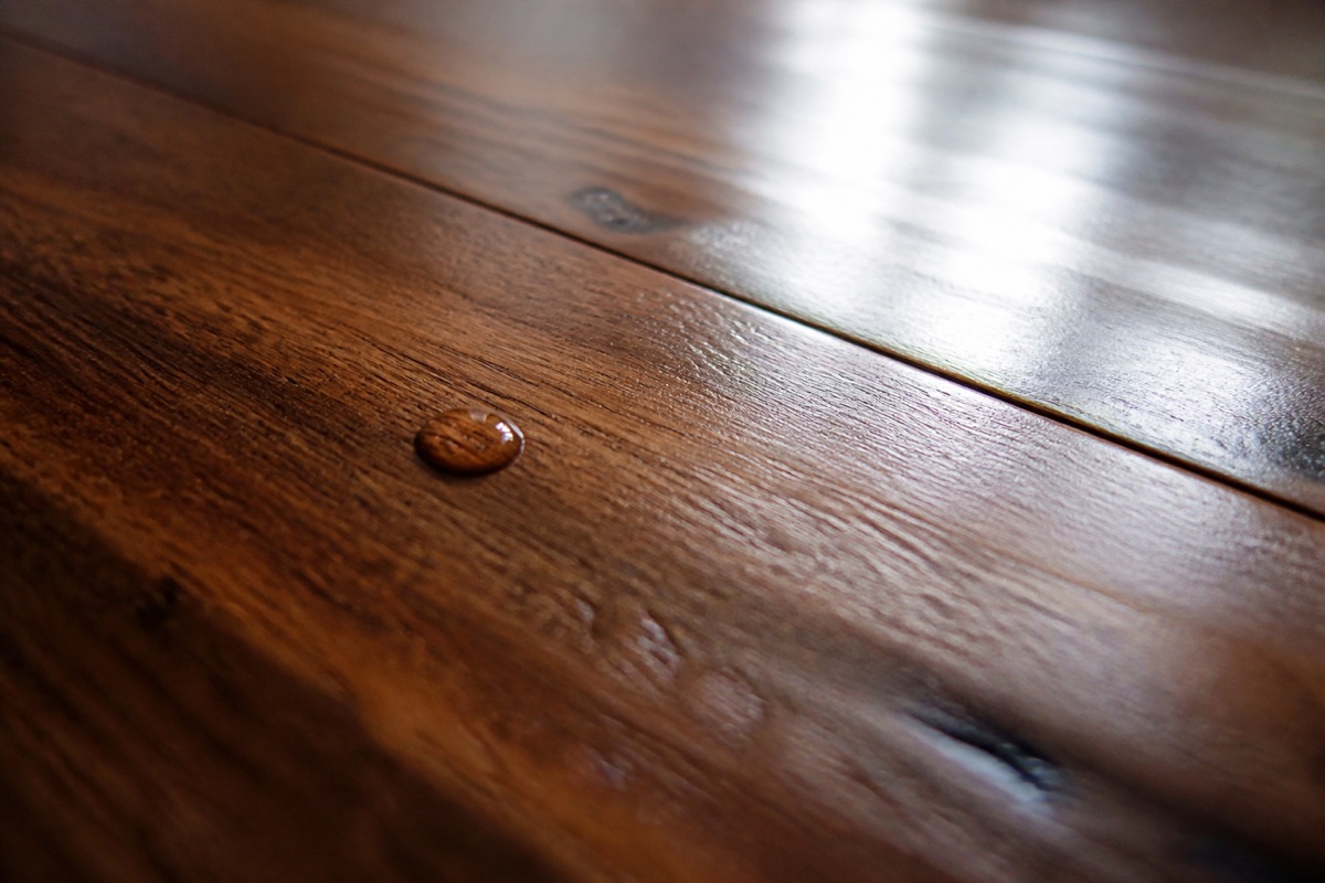 Close-up of a hardwood floor board at a low angle with a drop of water beaded on the satin finish